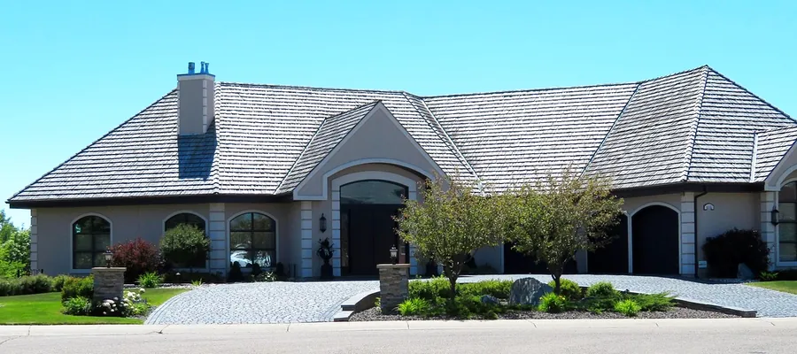 A single story home with freshly cleaned stucco walls, a spotless paver driveway and a trimmed lawn under a clear sky